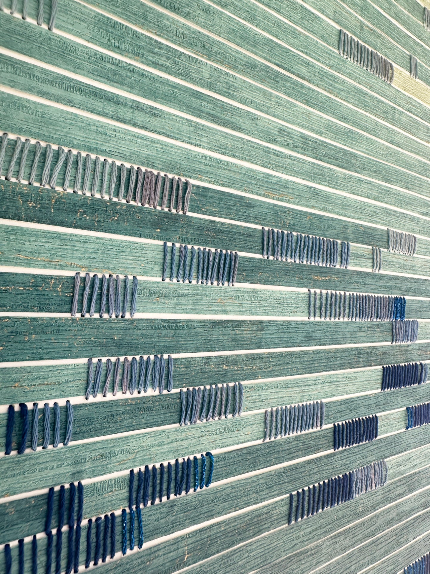 Close-up of a textured surface on coastal abstract art with horizontal lines and patterns in green and blue.