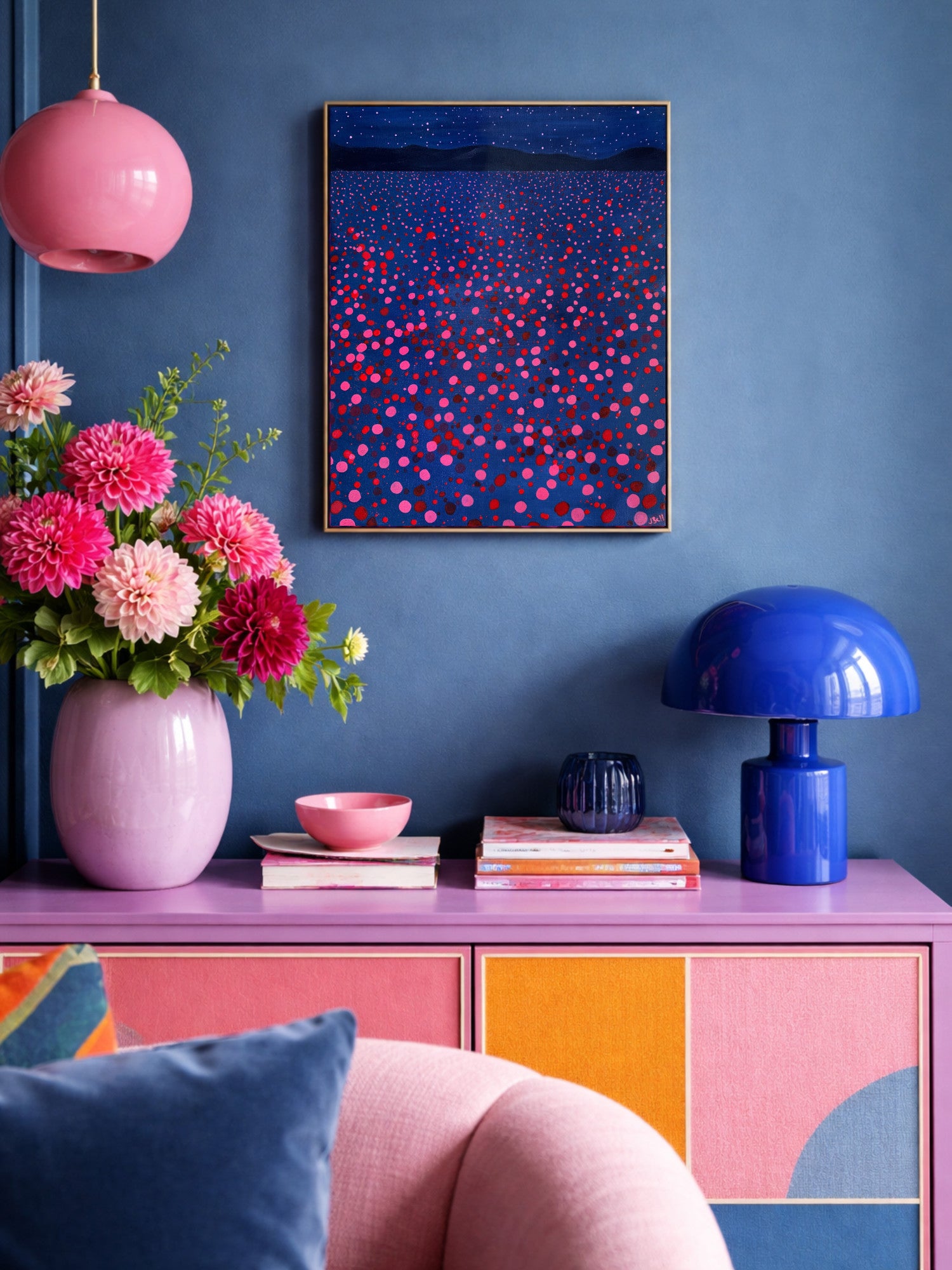 Colorful maximalist interior design with a pink vase, blue lamp, and abstract art on a blue wall.