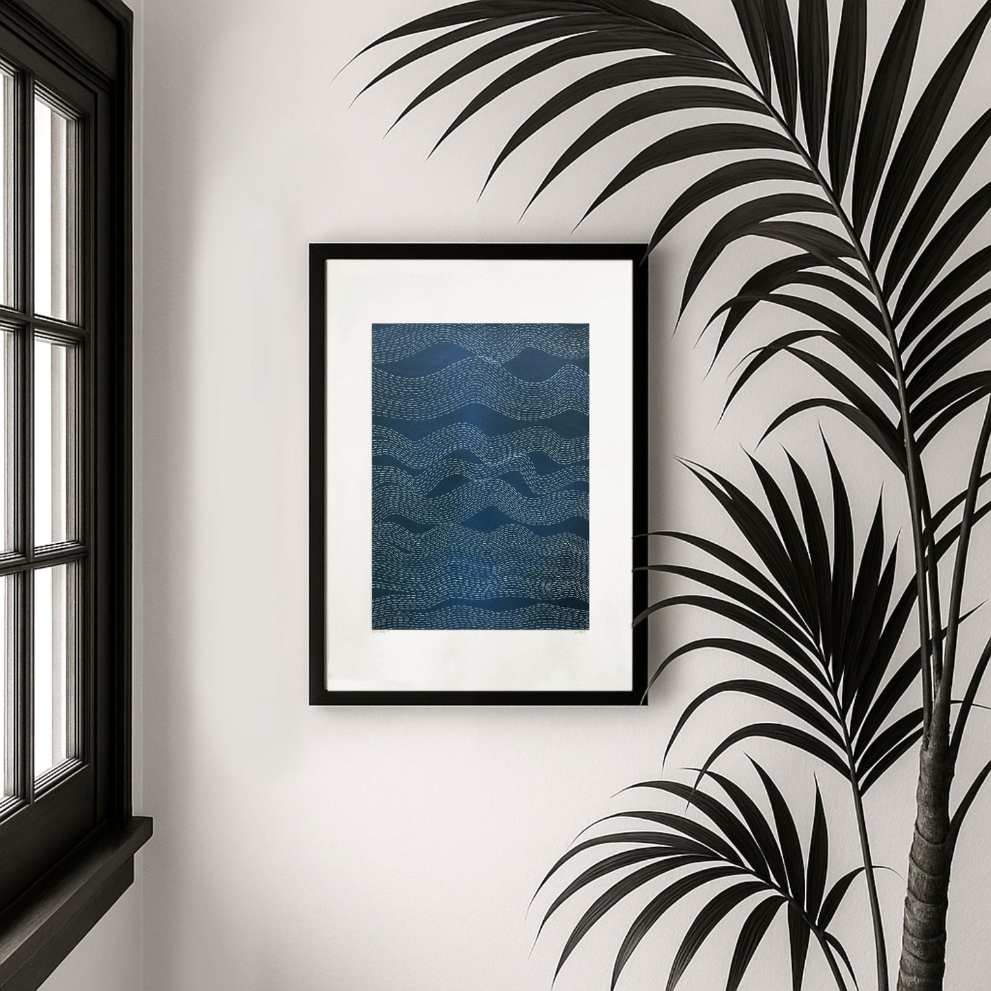 Framed blue abstract artwork on a wall with a window and palm leaves in the background