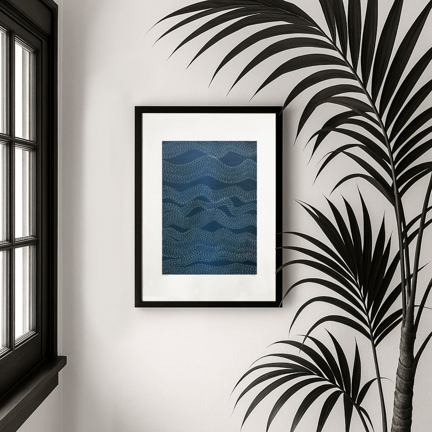 Framed blue abstract artwork on a wall with a window and palm leaves in the background