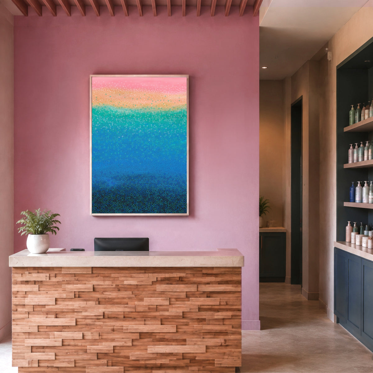 A framed abstract beach painting with pink, yellow, turquoise, and blue textured bands hangs on a dusty pink wall above a modern wooden reception desk in a spa-like interior.