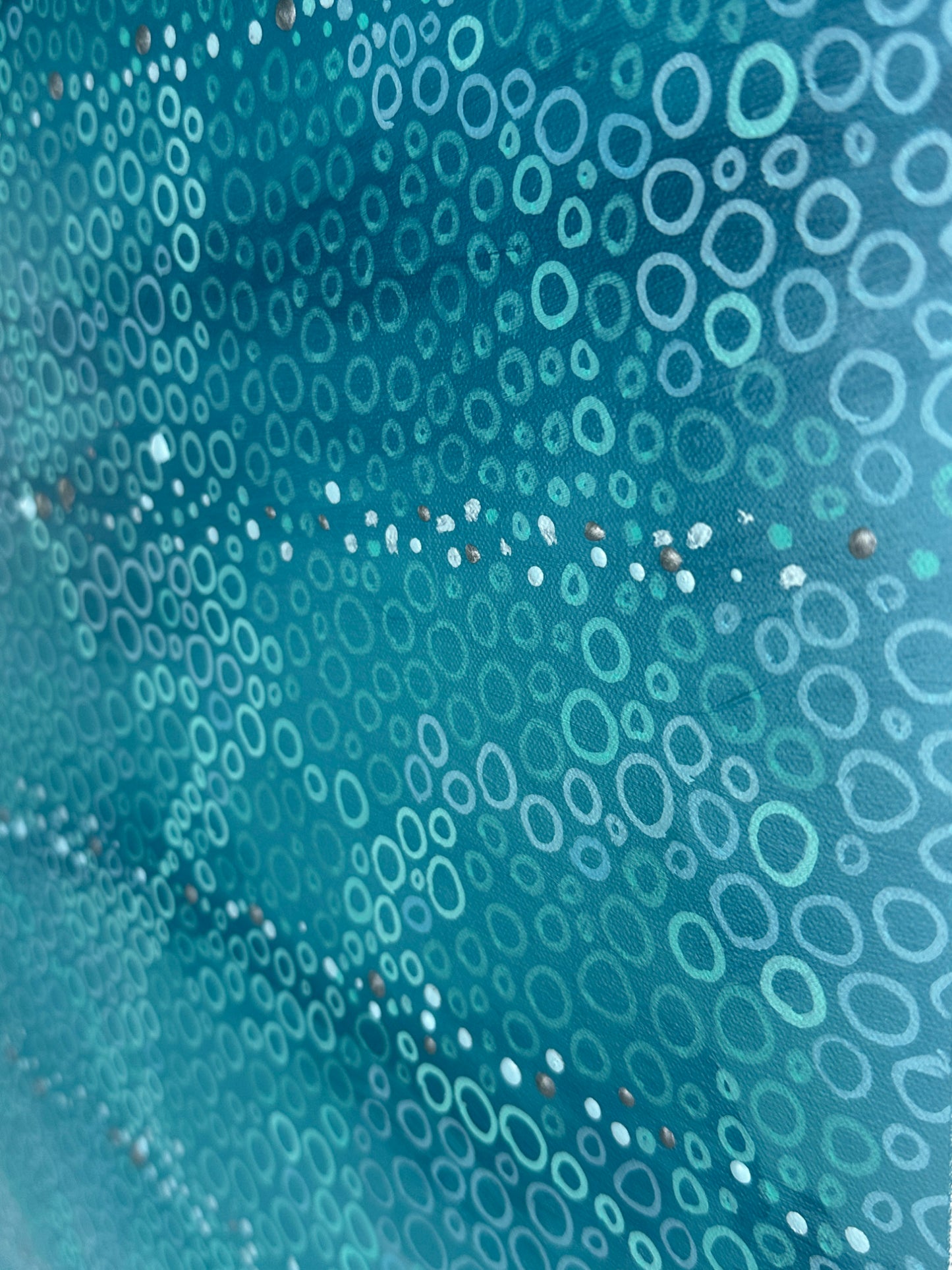 Close-up detail of a contemporary abstract painting showing hundreds of hand-painted circles in varying sizes layered over turquoise and blue tones. Fine metallic accents shimmer between the circular forms, revealing the texture and intricate mark-making of the original artwork.