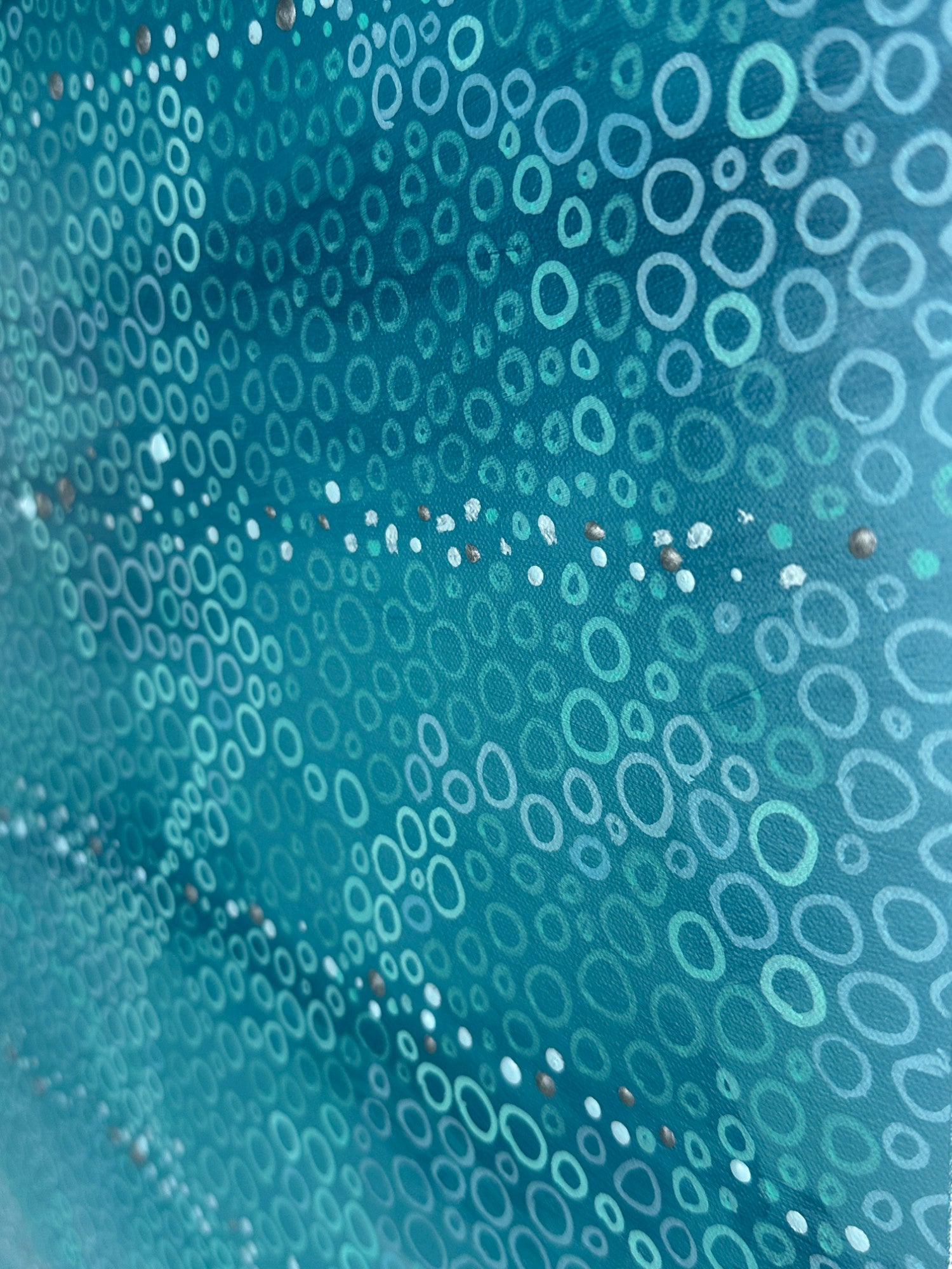 Close-up detail of a contemporary abstract painting showing hundreds of hand-painted circles in varying sizes layered over turquoise and blue tones. Fine metallic accents shimmer between the circular forms, revealing the texture and intricate mark-making of the original artwork.